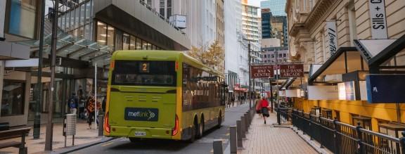 Light green Metlink bus drives down Lambton Quay during the day